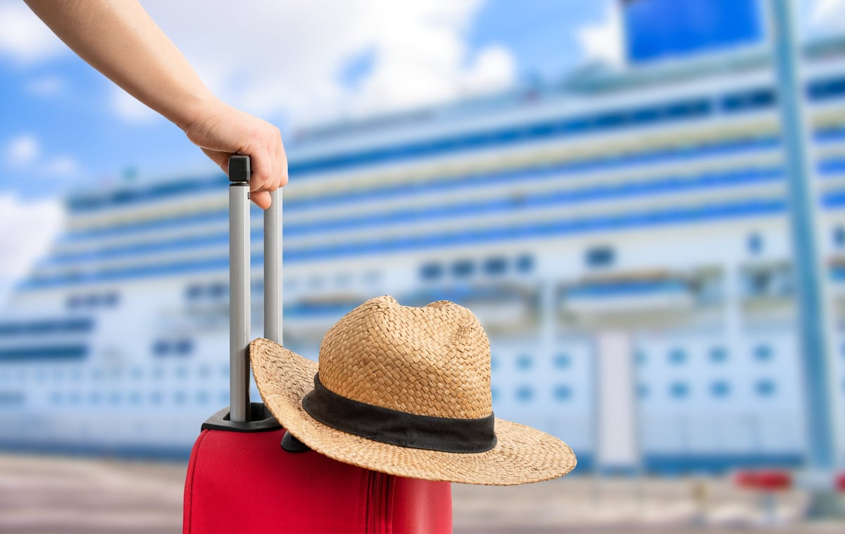 A red suitcase with a straw hat beside a cruise ship in port